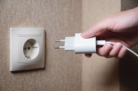 A young woman inserts a plug into a socket. A young woman plugs a charger or electrical appliance power cord into a socket. High quality photoの写真素材