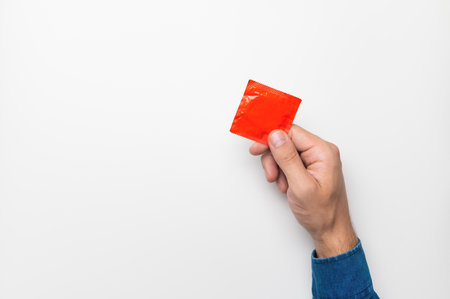male hand shows a red condom in a package on a white backgroundの写真素材