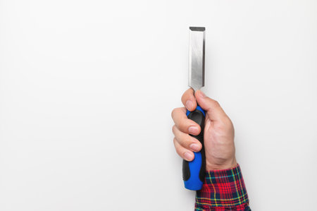 Close-up of a mans hand in a plaid shirt on a white background with a chisel, studio shotの写真素材