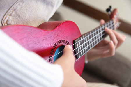 female gentle hands in which lies a red wooden ukulele, close-up. hipster girl hobby, at home