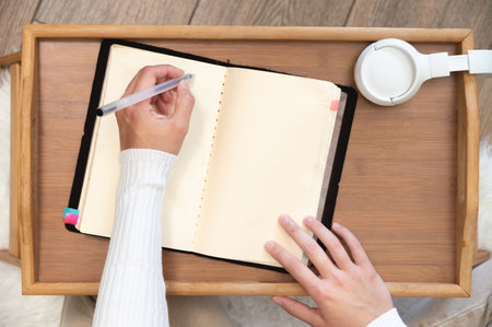 Top view Close-up of female hands writing with gel black pen in leather notepad on wooden table at homeの写真素材