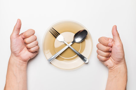 Male hands show a class gesture, a white table, an empty plate and a fork and a spoon lie on it, top view. delicious food ideaの写真素材