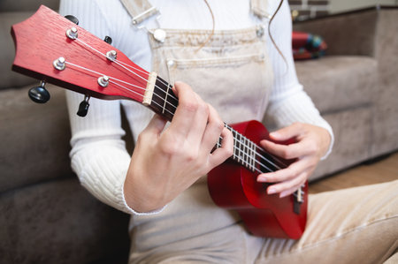 close-up, ukulele in female hands, hipster learns to play a musical instrument at home, sitting on the floor near the sofaの写真素材