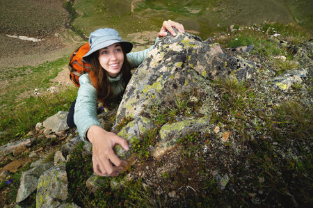 happy woman climbs a rock while trekking outdoors. carefree backpacker smiling at cameraの写真素材