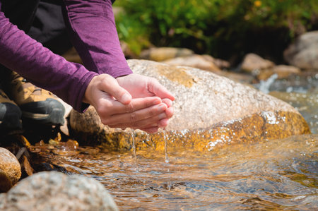 Close-up of water drops falling from female hands into a stream. The hand touches fresh water. A...