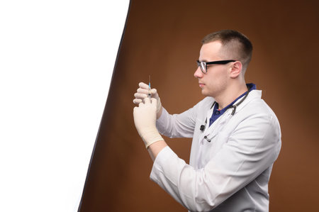 Portrait of young male doctor drawing Covid-19 vaccine from vaccine bottle, with syringe and stethoscope, Covid-19 vaccination conceptの写真素材