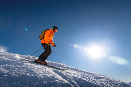 Professional skier athlete skiing at the top of a ski resort. Winter holidays and sports concept with adventure guy on the top of the mountain skiing down the slope.Warm bright sunny dayの写真素材