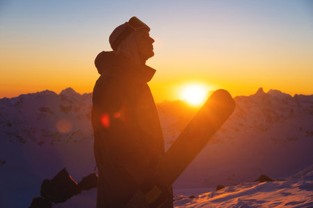 silhouette of a skier with skis standing on a slope at sunset against a mountain range. sportsman portraitの写真素材