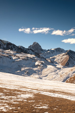 Daytime landscape of a snowy ridge with a mountain peak and yellow grass in the foreground
