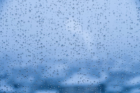 Natural water drops on glass. macro raindrops on the blue window of a car or house windowの写真素材
