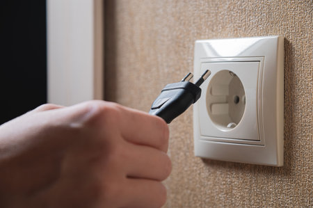 black cord with a plug from an electrical appliance is brought to the socket by hand, close-upの写真素材