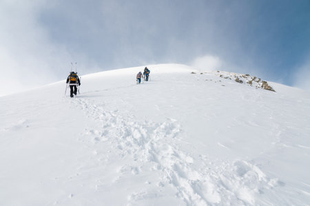 Mountaineers walking up along a snowy ridge with the skis in the backpack. Skier on the climbing track for freeride-descent. Backcountry skiers. ski free rider climbs the slope into deep snow powderの写真素材