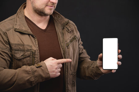Smiling man with big blank cell phone in hand showing white screen at camera pointing at you, recommending new app or mobile website, banner collage mockup, pointing finger at deviceの写真素材