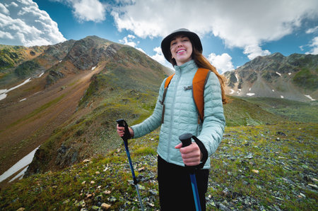 Portrait, the girl is happy and smiling while hiking in the mountains. Beautiful young caucasian sporty woman joyful stands with a backpack and looks at the cameraの写真素材