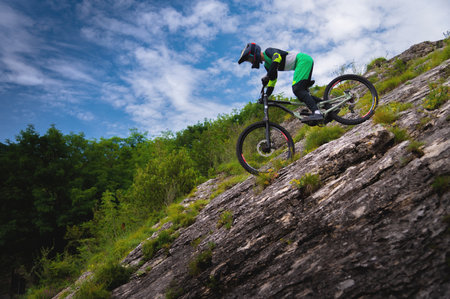 Downhill rider cyclist rides down a steep cliff surrounded by green trees against a blue sky. Copy space mtb conceptの写真素材