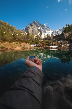A man with a compass in his hand in the high mountains against the backdrop of a clear lake. Travel concept. landscape photographyの写真素材