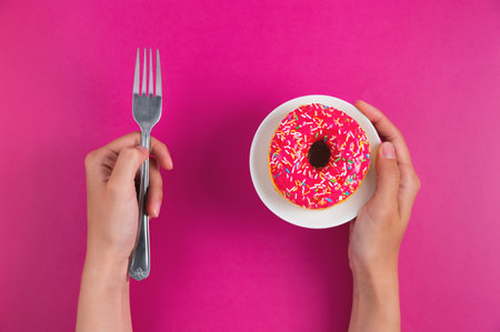 Breakfast concept. Close up, female hands with a fork and donut shape cookies on a pink background, top view, flat layの写真素材