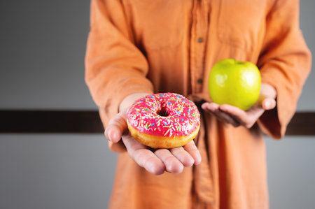 It is difficult to choose a healthy eating concept when a woman is holding a green apple and a donut with a lot of calories in her hand. Unrecognizable girl holding out a donutの写真素材