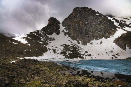 landscape of a high mountain, a mountain range in the snow with a lake in ice in the foreground....