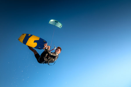 Sports kitesurfer in the air doing a trick with a wakeboard, rider in a wetsuit on a clear blue sky in a parachute jump, looking at the camera. Water sportsの写真素材