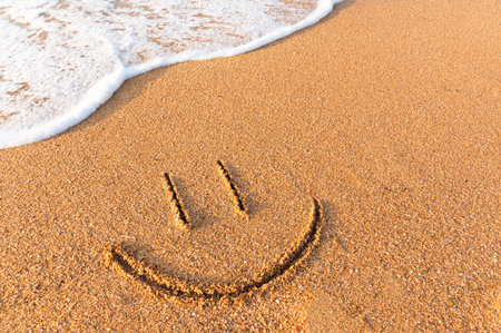 smile painted on the sand next to a foamy wave. Sandy beach with a friendly message written on itの写真素材