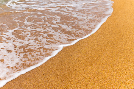 an ocean wave hits the sandy sand. Background with sea foam on golden sand beach, top viewの写真素材