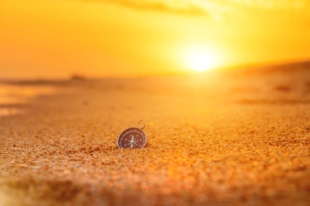 compass on the beach with sunrise or during sunset, orange sky with bright sun rays, travel concept