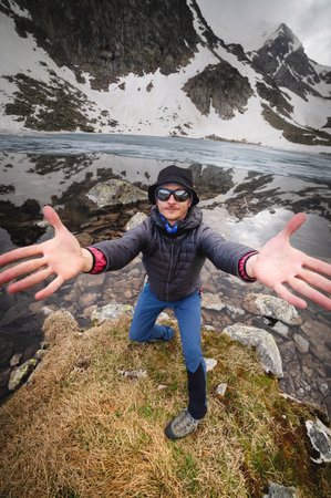 A Caucasian male mountain traveler in sunglasses and trekking clothes expressively invites you to...