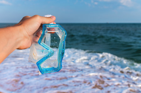 hand holds snorkeling goggles against the background of the sea or ocean and sky. Diving goggles and snorkeling equipment in hands near the beachの写真素材