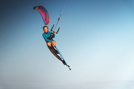 Caucasian woman kitesurfer athlete doing a trick in the air against a blue sky without a cloud. Professional kitesurfing trainingの写真素材