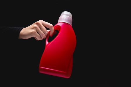 Close-up of a womans hand holding household chemicals, on a black background with copy space....