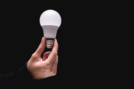 light bulb in hand on a black background. Close-up of a womans hand holding a light bulb. Studio...