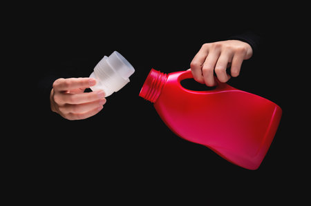 womans hand pours cleaning product or bleach on a black background. Woman opened detergent, close-up, label mockupの写真素材