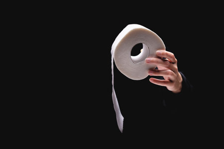 Close-up of a womans hand using toilet paper, against a dark background. A hand holds a roll of paper. White roll of toilet paper in a womans handの写真素材