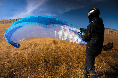 paraglider lands or rises on the yellow grass on a sunny day. A man after or before a paragliding flight. Glider with parachute, wide angle rear viewの写真素材