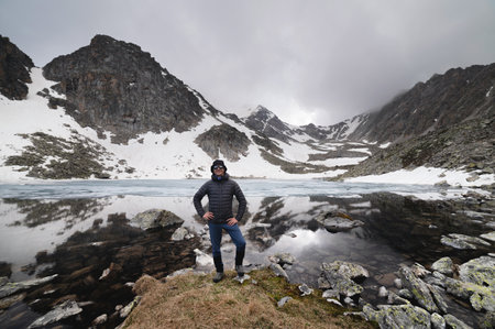 Happy active cheerful tourist in mountain sunglasses and a down jacket, joyful smiles expressively...