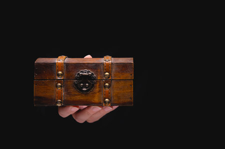 An old wooden box chest on a young female hand on a black background. Nice gift concept in gothic...