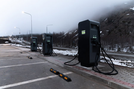 Electric car charging station, row of gas stations stands against the backdrop of mountains in fog in winter, cloudy weatherの写真素材