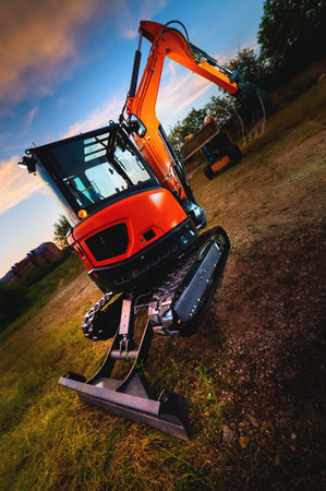 Mini bulldozer, small excavator against the backdrop of the sunset sky in the forest, wide angleの写真素材