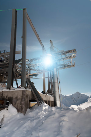 An unfinished metal structure of a cable car station high in the mountains. The structure is covered in snow and the sun shines through its ceilingsの写真素材