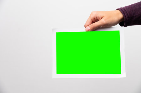 Paper photo in a womans hand on a white background. Blank mockup green screen for inserting a photoの写真素材