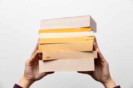 Stack of books in hand, Book Day, several books in hands on neutral white background. Home leisure. Self-isolation home, home schoolingの写真素材