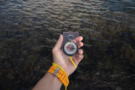 First person view of a mans hand holding a compass against a beautiful seascape. Navigation concept of finding your own way and orientation to the cardinal pointsの写真素材