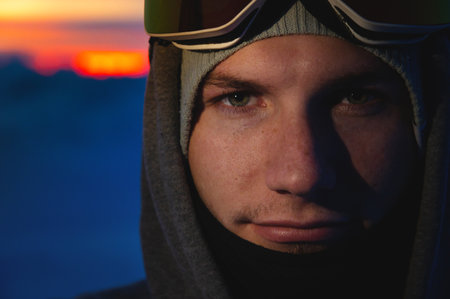 Male model standing relaxed in mountains at sunset or sunrise wearing hat, close up of faceの写真素材