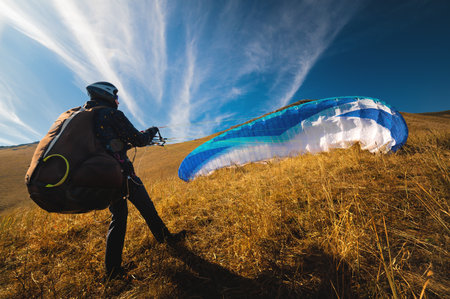 paraglider prepares for a paragliding flight or has already completed it and landed, standing on a hill in the grass, surrounded by a vibrant autumn landscapeの写真素材