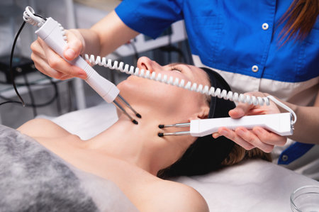 Happy woman gets ultrasonic facial massage with ultrasonic facial machine. Woman undergoing electric...