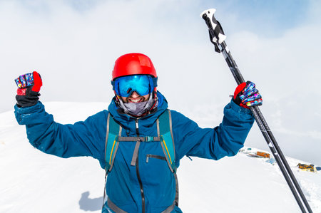 Young man standing in snow with raised hands and ski poles, joy and happiness on the face of the guy who climbed the mountainの写真素材
