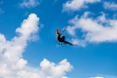 A person performs a trick with a grab against the background of a blue sky and cloudsの写真素材