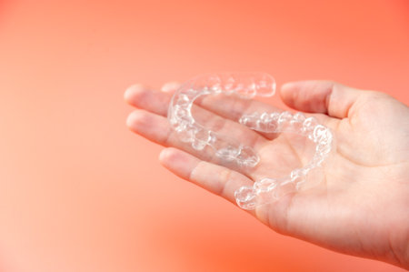 Close up top view female hand holding dental aligner retainer on palm for dental treatment. Shot indoor in studio on pink backgroundの写真素材