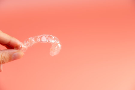 Hand holding plastic braces on pink background. Female hand showing modern methods of teeth straighteningの写真素材
